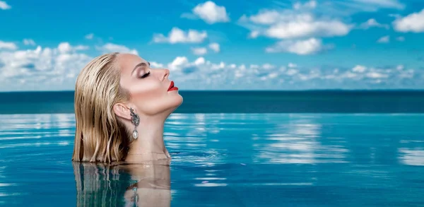 Modelo de mulher loira bonita com cabelo molhado e maquiagem elegante sentado em uma piscina com vistas incríveis em um hotel de luxo, vestindo jóias, brincos com os cristais e corpo nu molhado — Fotografia de Stock