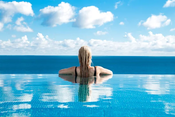 Belle femme blonde modèle aux cheveux mouillés et élégant maquillage assis dans une piscine avec une vue imprenable dans un hôtel de luxe, portant des bijoux, des boucles d'oreilles avec les cristaux et le corps nu humide — Photo