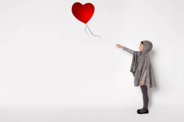 Korkmuş küçük bir kız beyaz bir arka plan üzerinde duruyor ve rüzgar tarafından kaçtı balon sonra elini tutar