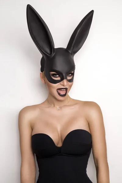 Donna sexy con grandi seni che indossano una maschera nera Coniglietto di Pasqua in piedi su uno sfondo bianco e guarda molto sensualmente — Foto Stock