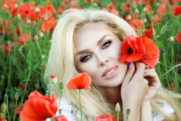 Güzel sarışın uzun saçlı ve kırmızı haşhaş bir çayır üzerinde duran bir şapka