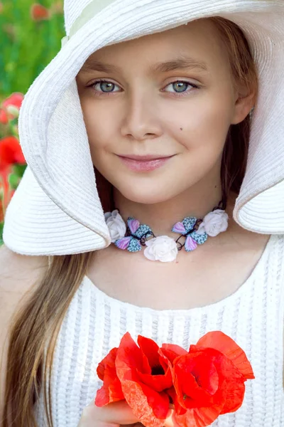 Sladká holčička v klobouku, stojící na louce a drží červené vlčí máky — Stock fotografie