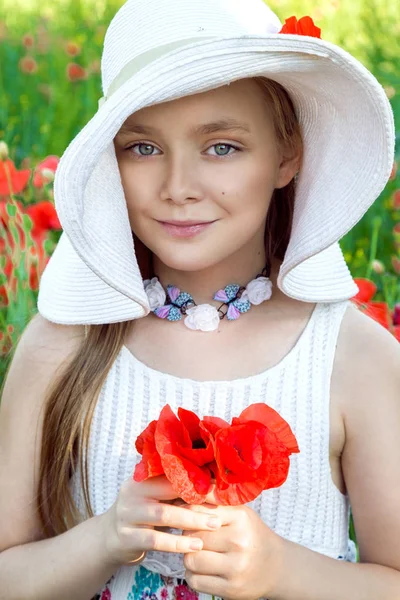 Sladká holčička v klobouku, stojící na louce a drží červené vlčí máky — Stock fotografie