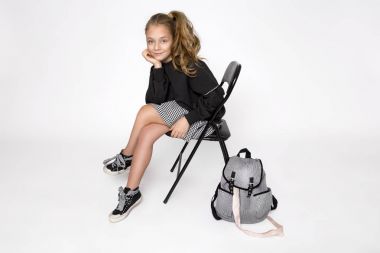 Sevimli küçük kız okul kıyafetleri ve okul sırt çantası beyaz arka plan üzerinde oturan giymiş