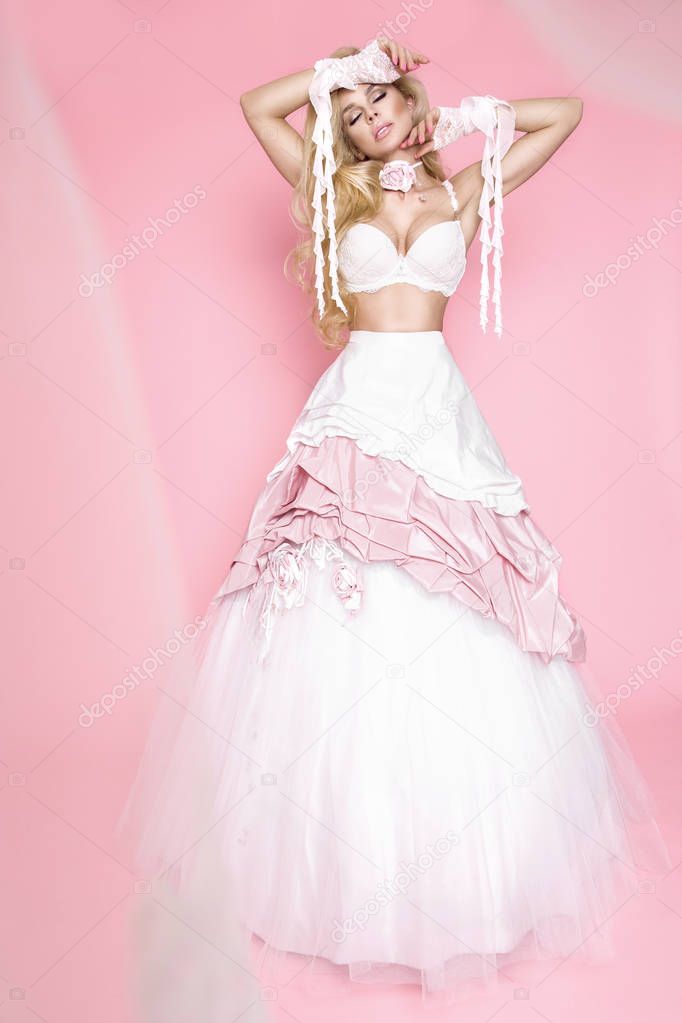 Beautiful blonde female model in a wedding dress on a pink background