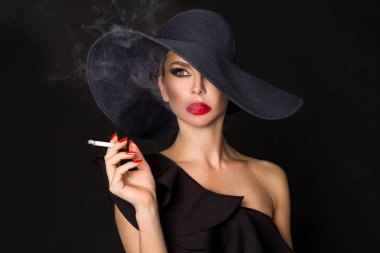 Zarif kadın, femme fatale siyah şapka ile sigara elinde. Siyah arka plan üzerine