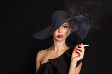 Zarif kadın, femme fatale siyah şapka ile sigara elinde. Siyah arka plan üzerine