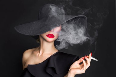 Zarif kadın, femme fatale siyah şapka ile sigara elinde. Siyah arka plan üzerine