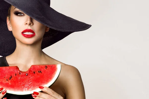 Hermosa modelo femenina con cara perfecta y sombrero rojo sosteniendo una sandía en su cara — Foto de Stock