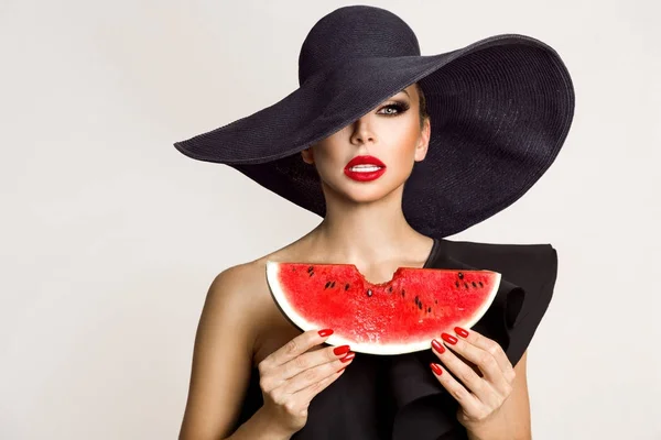 Schöne weibliche Modell mit perfektem Gesicht und rotem Hut hält eine Wassermelone vor ihrem Gesicht — Stockfoto