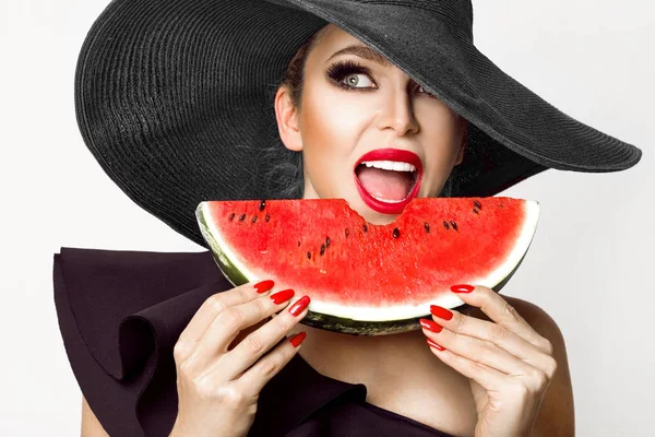 Modelo feminino bonito com rosto perfeito e chapéu vermelho segurando uma melancia em seu rosto — Fotografia de Stock