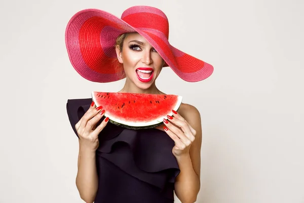 Hermosa modelo femenina con cara perfecta y sombrero rojo sosteniendo una sandía en su cara — Foto de Stock