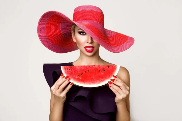 Modelo feminino bonito com rosto perfeito e chapéu vermelho segurando uma melancia em seu rosto — Fotografia de Stock