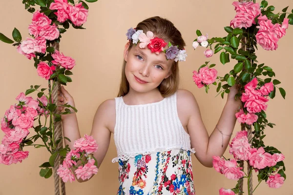 Doce, linda menina com uma grinalda de flores na cabeça, balançando em um balanço — Fotografia de Stock