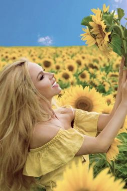 Ayçiçeği ile bir çayır üzerinde duran ve sonsuza dek mutlu gülümseyen güzel sarışın kadın