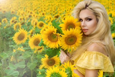 Ayçiçeği ile bir çayır üzerinde duran ve sonsuza dek mutlu gülümseyen güzel sarışın kadın