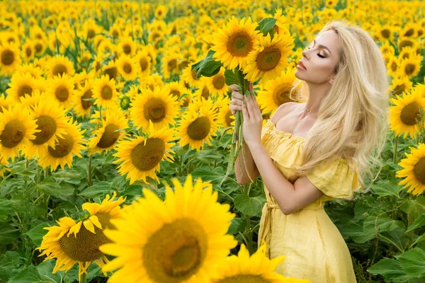 Mulher loira bonita de pé em um prado com girassóis e sorrindo feliz — Fotografia de Stock