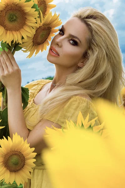 Krásná blondýna žena stojící na louku s slunečnice a šťastně se usmívala — Stock fotografie