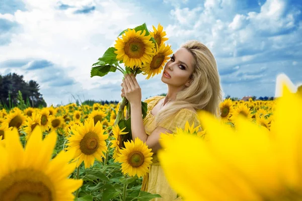 Mulher loira bonita de pé em um prado com girassóis e sorrindo feliz — Fotografia de Stock