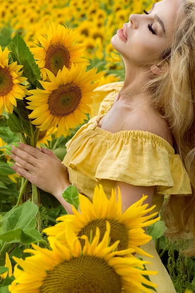 Mulher loira bonita de pé em um prado com girassóis e sorrindo feliz — Fotografia de Stock