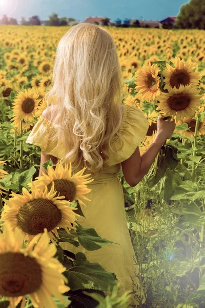 Όμορφη ξανθιά γυναίκα στέκεται σε ένα λιβάδι με ηλιοτρόπια και χαμογελώντας ευτυχώς — Φωτογραφία Αρχείου