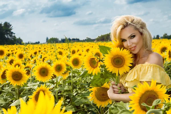 Mulher loira bonita de pé em um prado com girassóis e sorrindo feliz — Fotografia de Stock