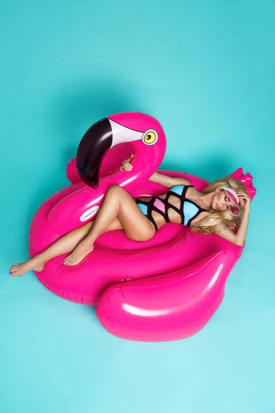 Splendida modella bionda sexy in bikini colorato, si trova su un fenicottero rosa — Foto Stock