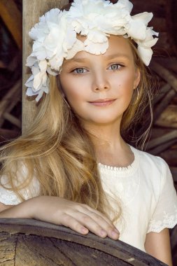 Çiçek çelenk kafasındaki bir Batı kasabası arka plan üzerinde duran küçük sevimli küçük kız