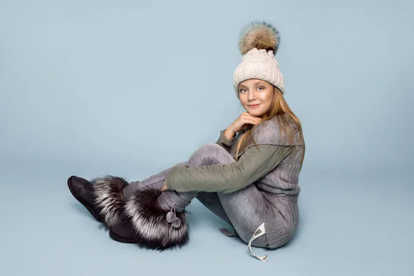 Söt liten flicka klädd i vinterkläder, hatt och vinter jacka med päls, stående på blå bakgrund — Stockfoto