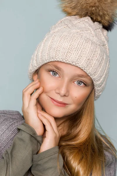 Linda niña vestida con ropa de invierno, sombrero y chaqueta de invierno con piel, de pie sobre fondo azul —  Fotos de Stock