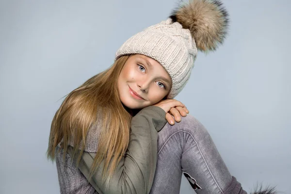 Jolie petite fille vêtue de vêtements d'hiver, chapeau et veste d'hiver avec fourrure, debout sur fond bleu — Photo