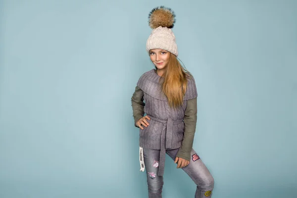 Linda niña vestida con ropa de invierno, sombrero y chaqueta de invierno con piel, de pie sobre fondo azul — Foto de Stock