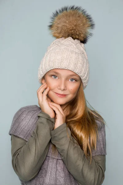 Милая маленькая девочка одета в зимнюю одежду, шляпу и зимнюю куртку с мехом, стоя на синем фоне — стоковое фото