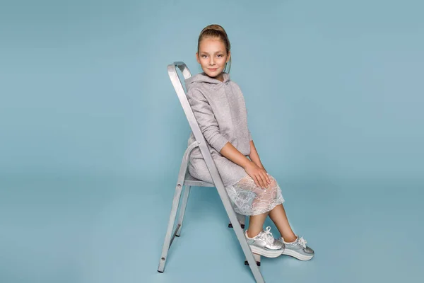 Linda niña vestida con ropa de escuela y mochila escolar de pie sobre fondo azul — Foto de Stock