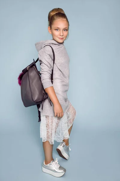 Linda niña vestida con ropa de escuela y mochila escolar de pie sobre fondo azul —  Fotos de Stock