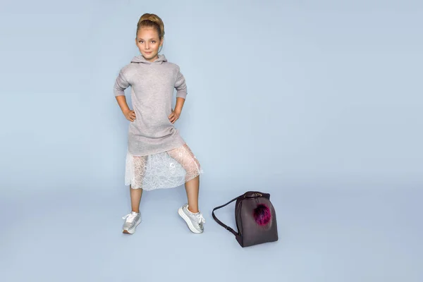 Ładna dziewczynka ubrana w szkole ubrania i szkolny plecak stojąc na niebieskim tle — Zdjęcie stockowe