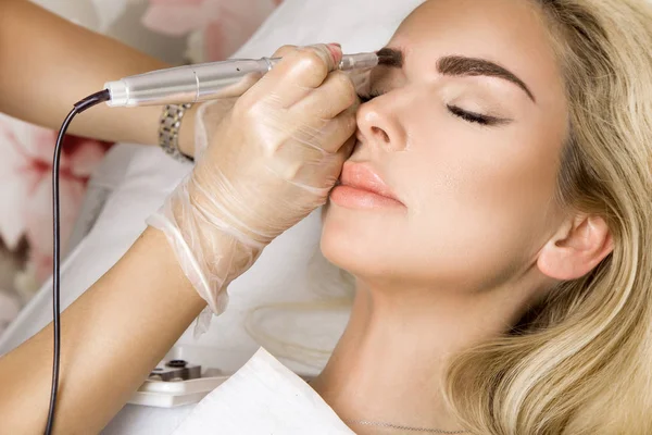 Beautiful woman with smooth, young skin, sitting in a beautician. A beautician performs modeling permanent eyebrows makings. — Stock Photo, Image