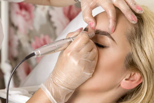 Beautiful woman with smooth, young skin, sitting in a beautician. A beautician performs modeling permanent eyebrows makings. — Stock Photo, Image
