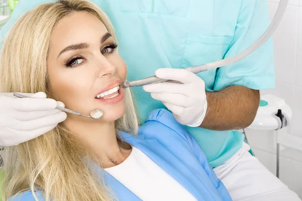 Mulher bonita nova com dentes brancos bonitos sentados em uma cadeira dental. O dentista cura os dentes. . — Fotografia de Stock