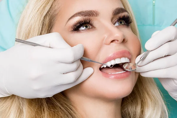 Mulher bonita nova com dentes brancos bonitos sentados em uma cadeira dental. O dentista cura os dentes. . — Fotografia de Stock