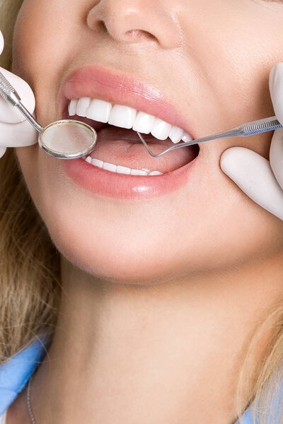 Молодая красивая женщина с красивыми белыми зубами сидит на стоматологическом стуле. Зубной врач лечит ее зубы
.