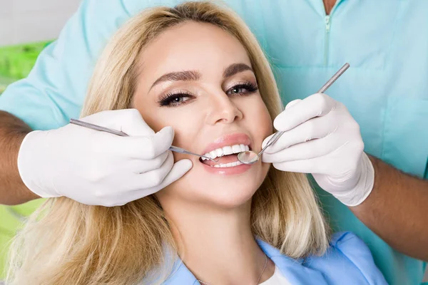 Ung vacker kvinna med vackra vita tänder som sitter på en stol. Tandläkaren botar hennes tänder. — Stockfoto