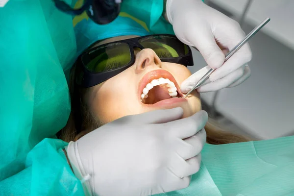 Mooie jongedame met mooie witte tanden, zittend op een tandheelkundige stoel. De tandarts geneest haar tanden. — Stockfoto