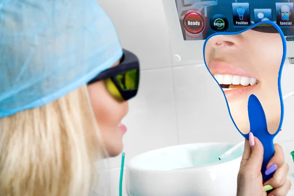Mujer hermosa joven con hermosos dientes blancos sentados en una silla dental. El dentista cura sus dientes . — Foto de Stock