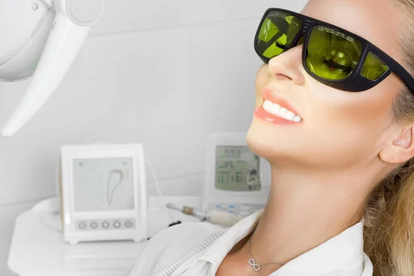 Fiatal gyönyörű nő gyönyörű fehér fogak, a fogorvosi székben ül. A fogorvos meggyógyítja a fogát. — Stock Fotó
