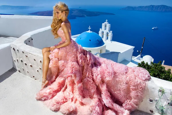 素晴らしいウェディング ドレスの美しい花嫁金髪女性モデルは、ギリシャのサントリーニ島にポーズし、向こうには美しい景色を — ストック写真