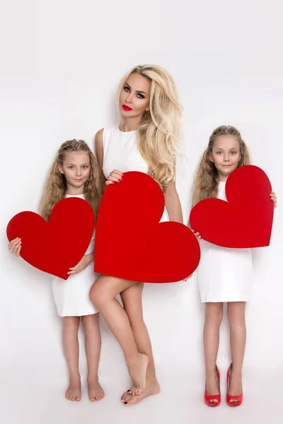 Piękna Blondynka kobieta matka i Córka, stojąc na białym tle i przytrzymując czerwone serce w jego rękach — Zdjęcie stockowe