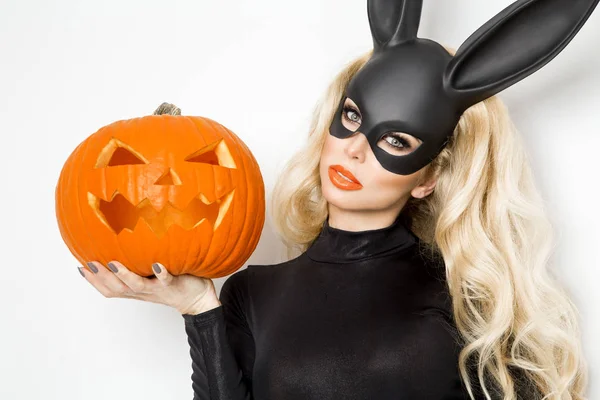 Bella giovane donna in costume coniglietto di Halloween, in piedi accanto a cesto pasquale e tenendo zucca — Foto Stock