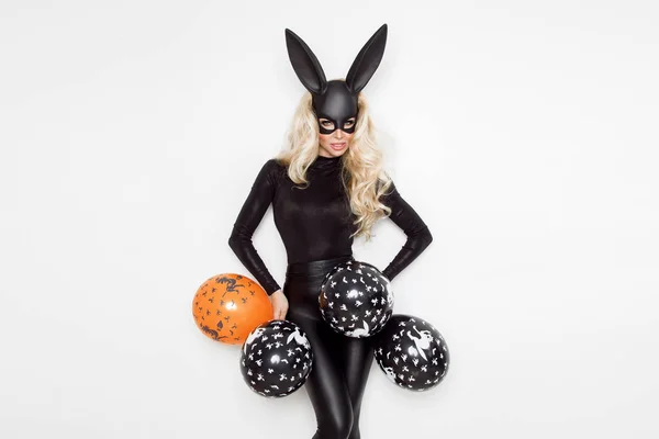 Mooie jonge vrouw in Halloween bunny kostuum, staande op een witte achtergrond en houden ballonnen — Stockfoto