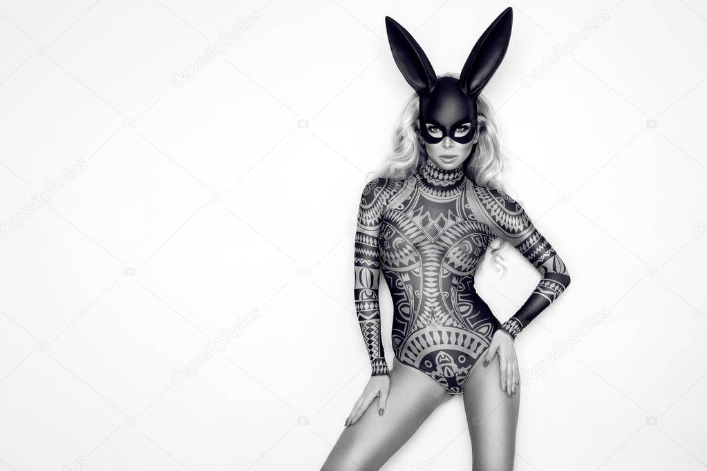 Beautiful young woman in Halloween, tattoo costume and black bunny  mask, standing on white background